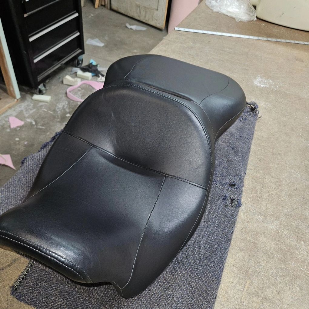 Black motorcycle seat on a gray carpeted floor in a workshop.