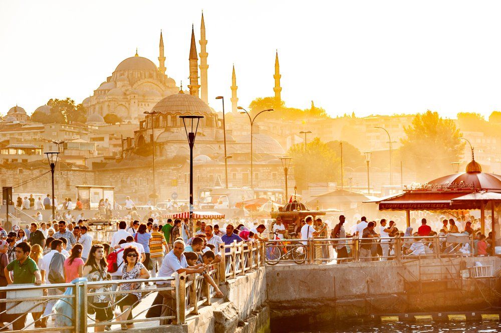 A large group of people are standing on a pier in front of a mosque.