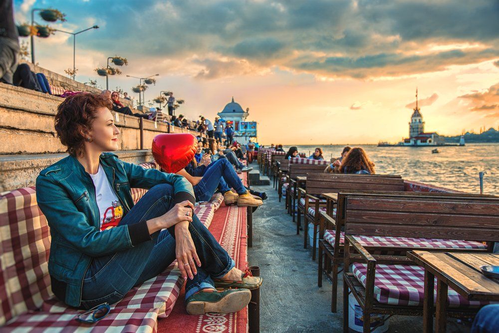 A woman is sitting on a couch in front of a body of water.