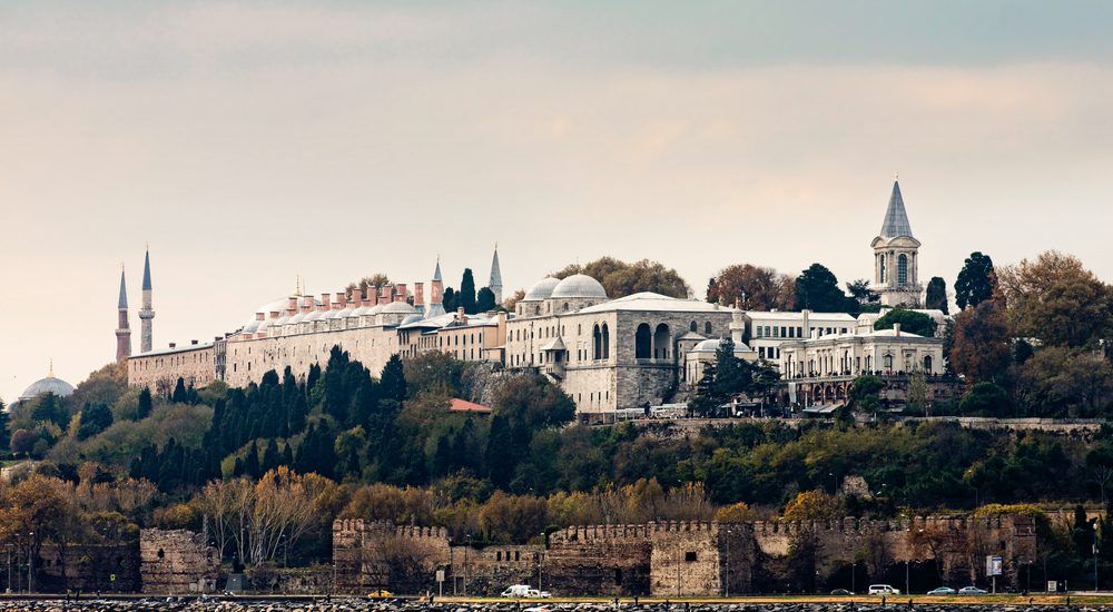 A large building is sitting on top of a hill next to a body of water.