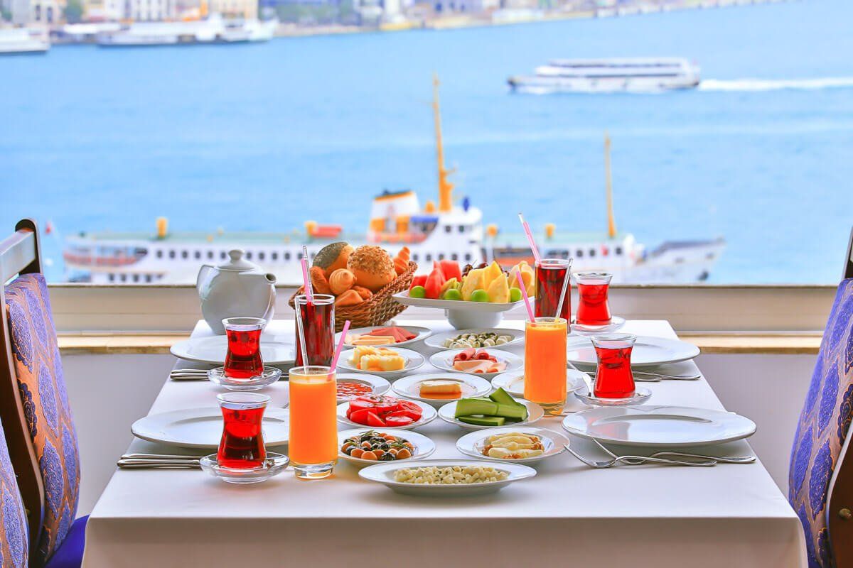 A table topped with plates of food and drinks with a view of the ocean.