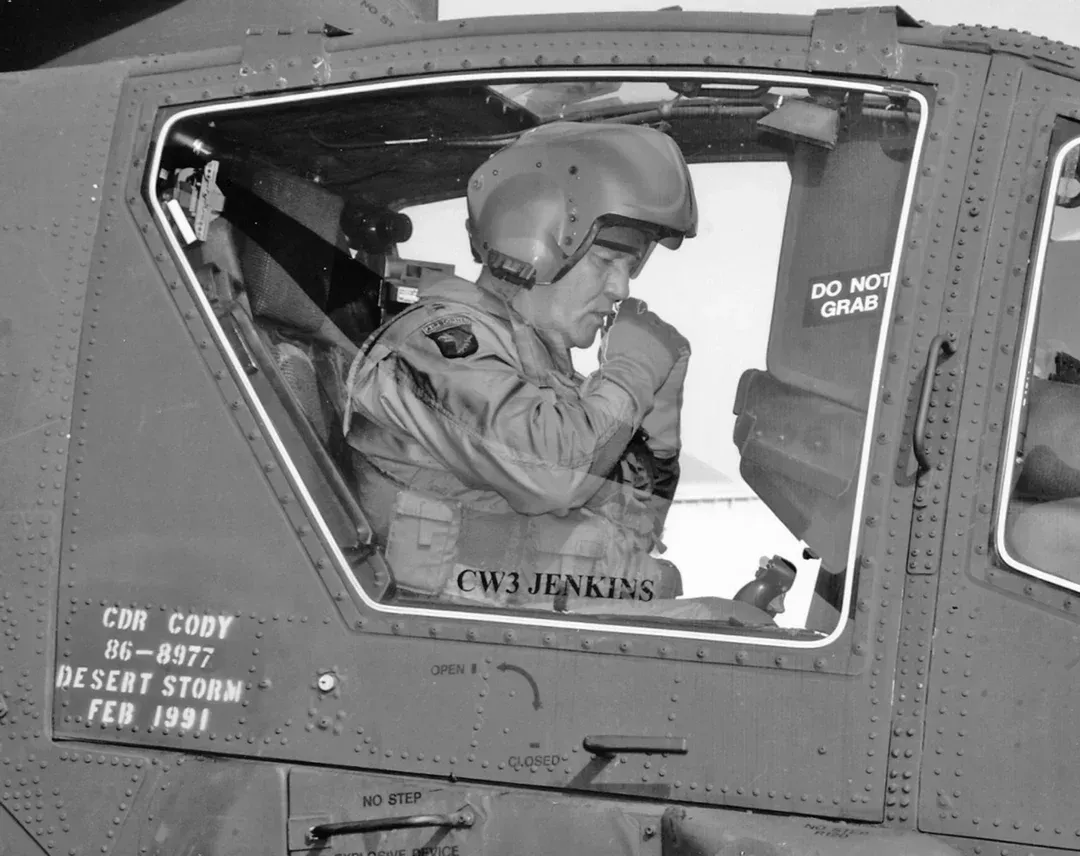 Pilot in cockpit wearing a helmet, adjusting equipment. Black and white photo,
