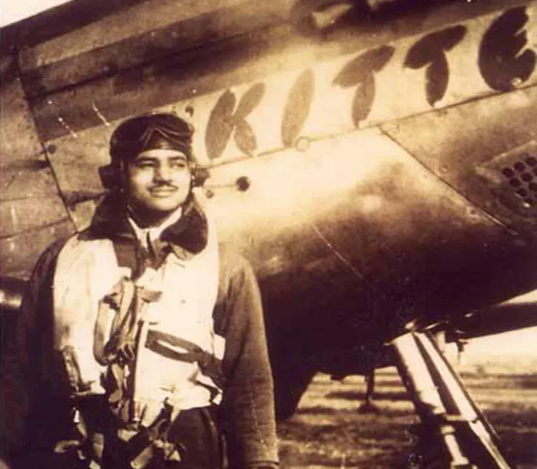 Man in flight gear stands near a biplane labeled
