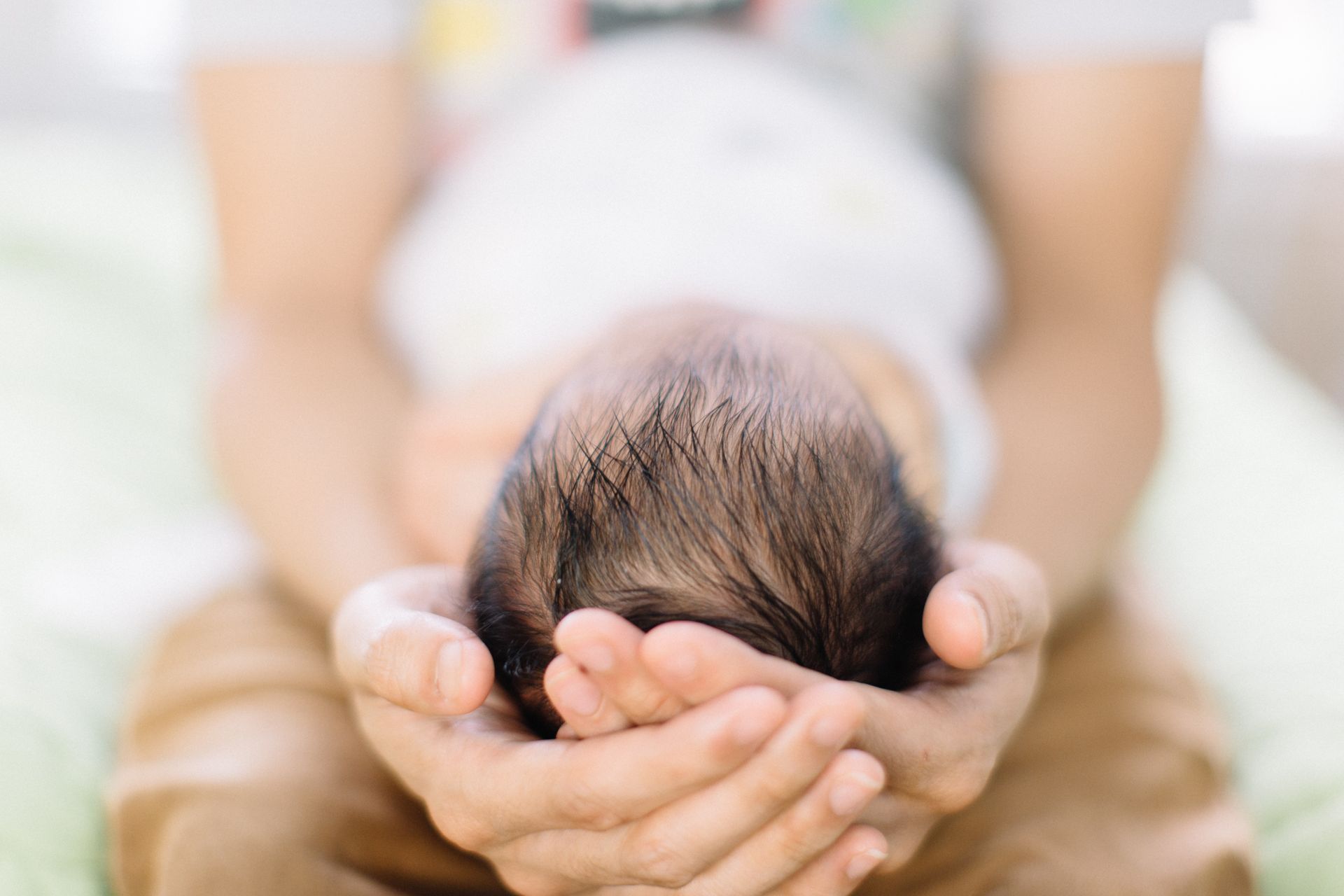 Person holding a newborn baby, head resting in cupped hands. Dark hair, light skin.