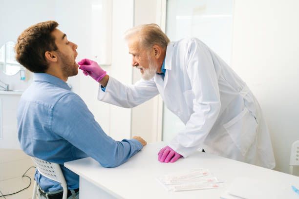 Doctor examining a patient's throat in a medical office. The doctor wears a white coat and pink gloves.