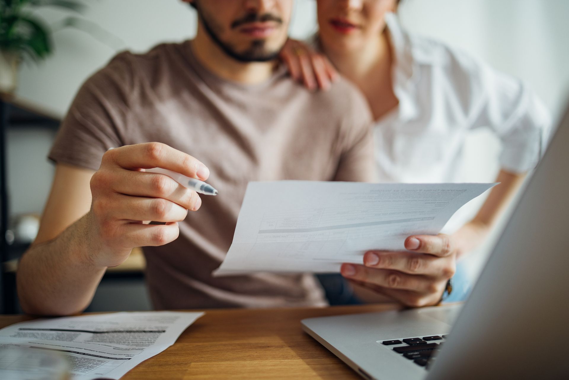 Man reviewing documents with woman looking on; home setting.