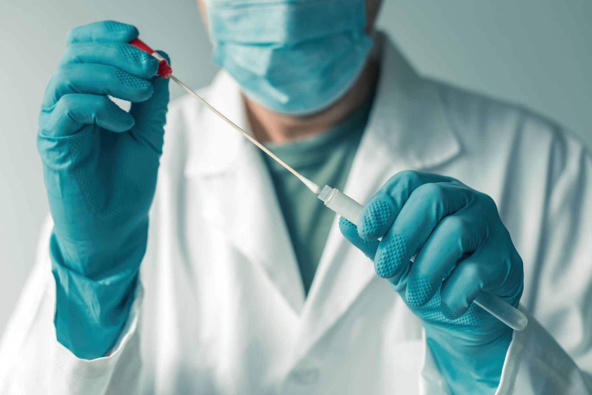 Doctor in a lab coat and mask holding a swab and vial, preparing for a medical test.