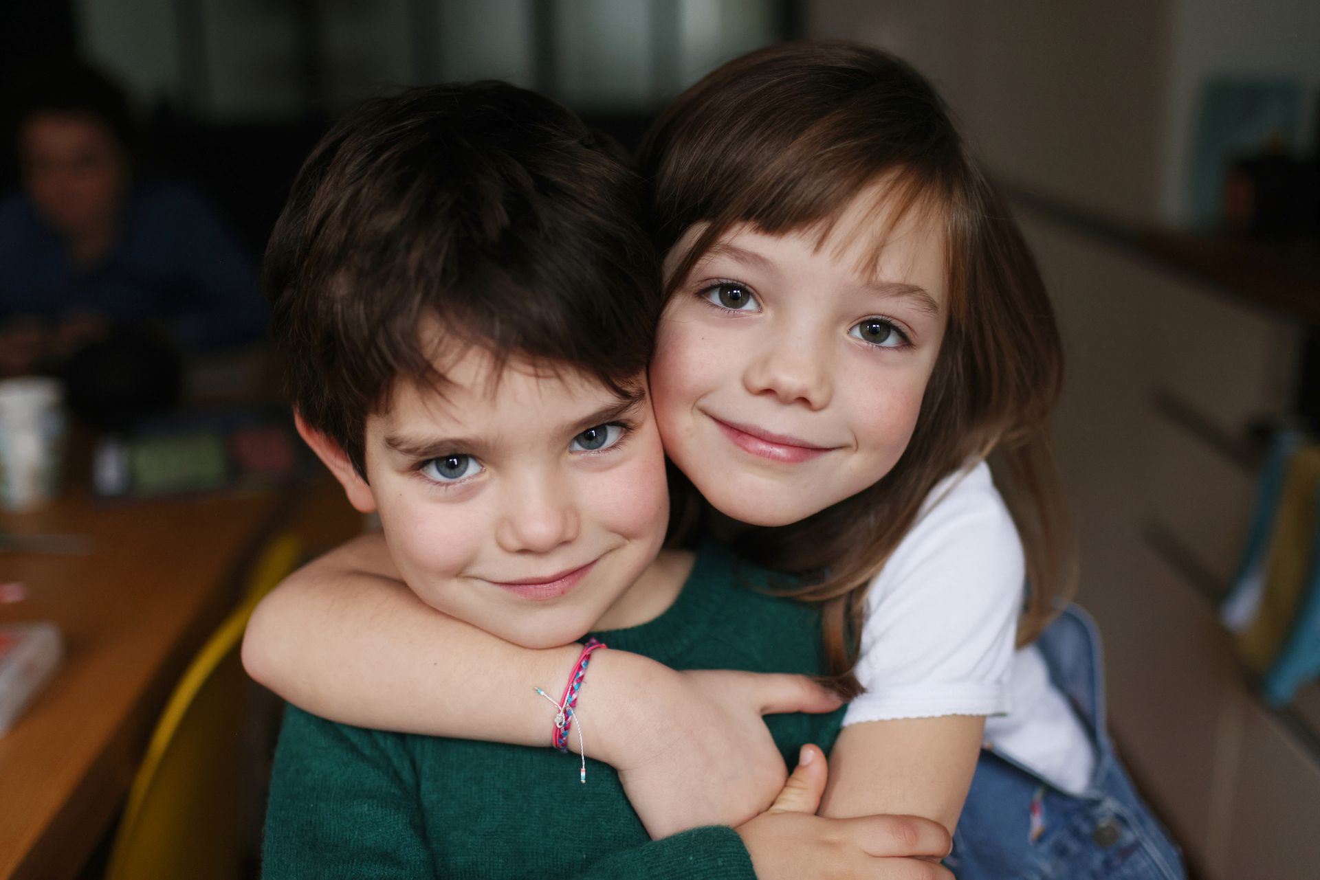 Boy and girl embrace, smiling. Boy in green, girl in white, indoors.