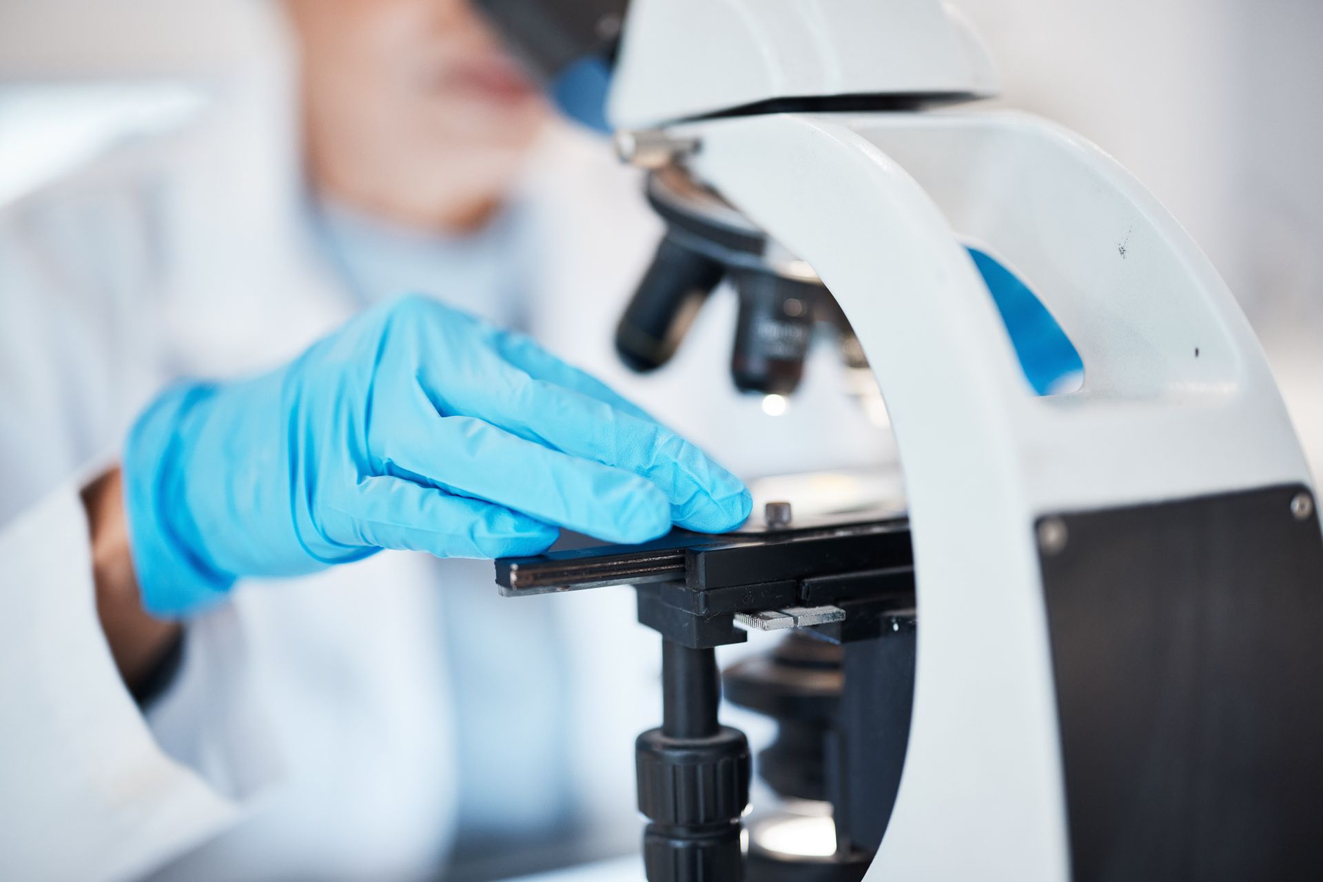 Scientist in blue gloves adjusts a microscope slide, likely in a lab setting.