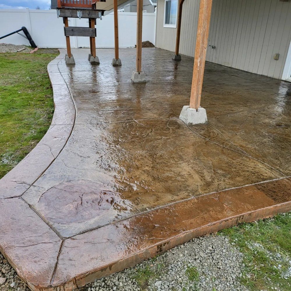 Wet, stained concrete patio with a decorative border, under a wooden deck supported by posts.