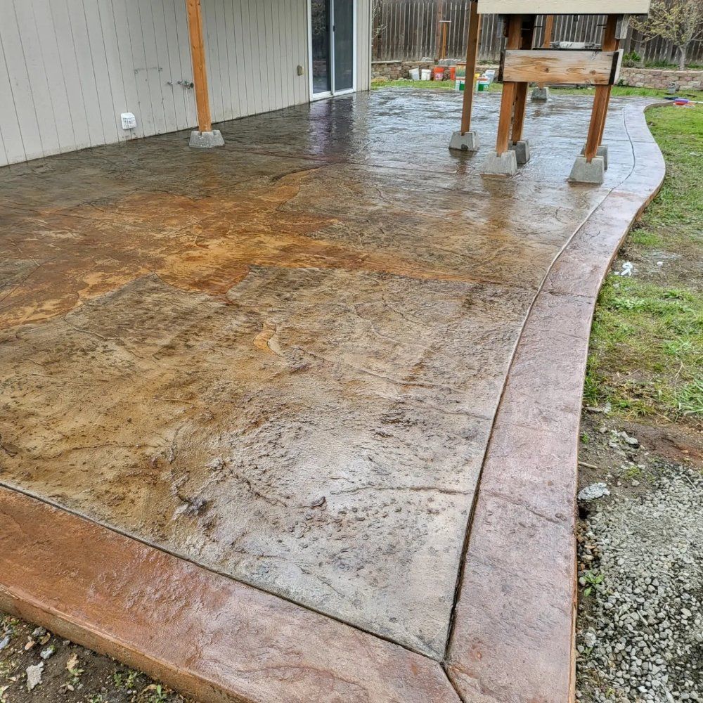 Wet, stamped concrete patio with a dark brown border. A grill sits nearby.