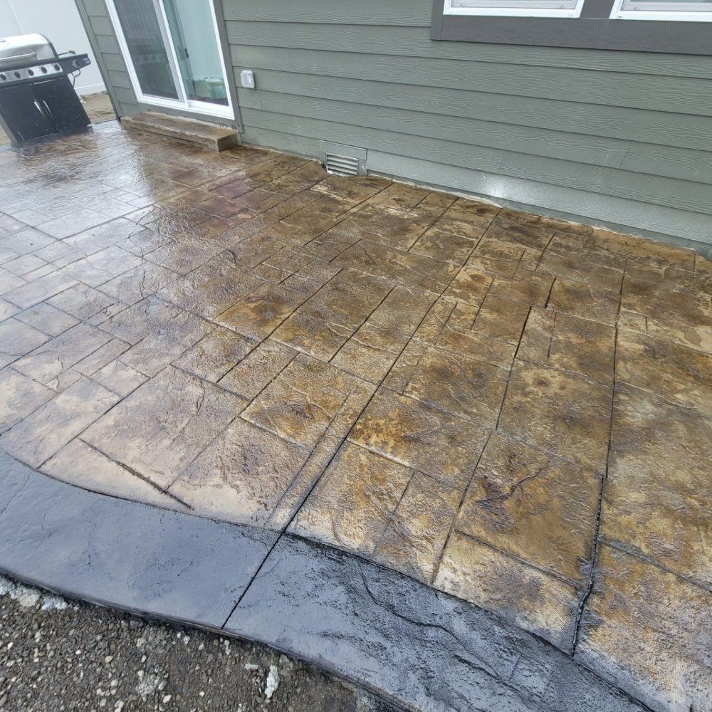 Stamped concrete patio with a dark grey border next to a house with a grill visible.