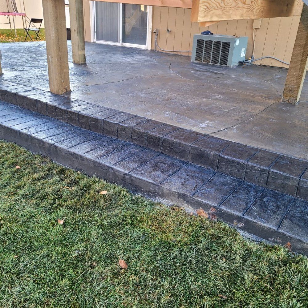 Concrete steps lead to a patio under a wooden structure. The steps have a textured pattern.