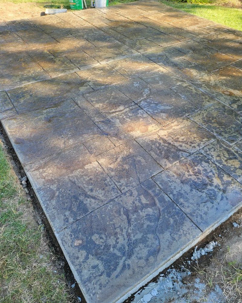 Stamped concrete patio, dark gray, with a stone pattern, in a grassy yard.