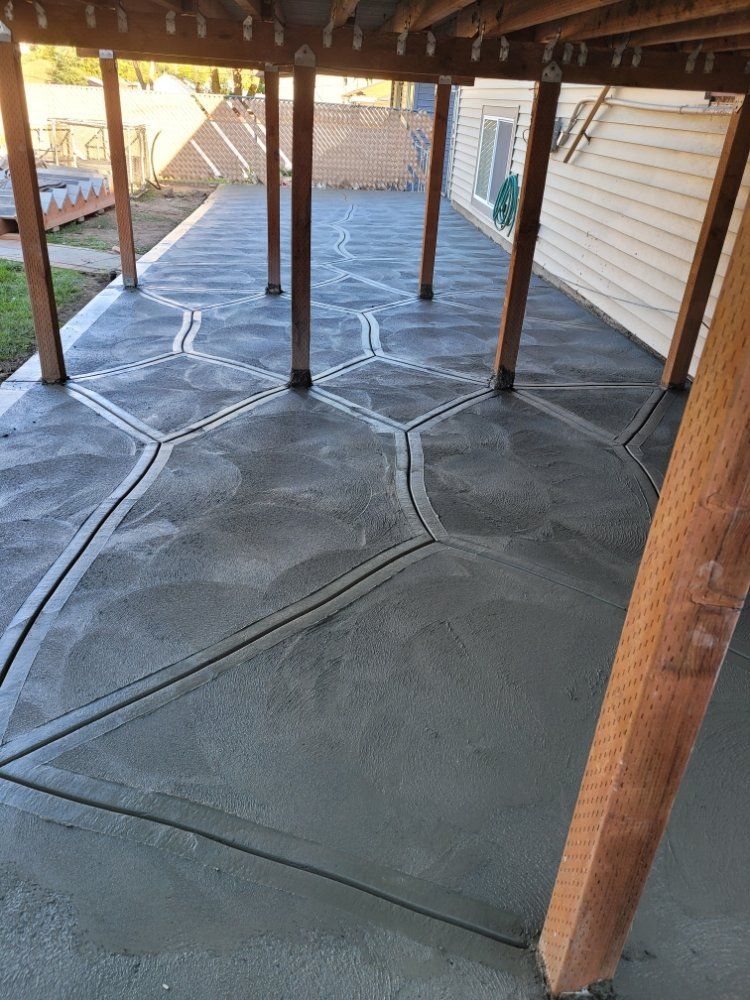 Freshly poured gray concrete patio with geometric design, beneath a wooden deck structure.