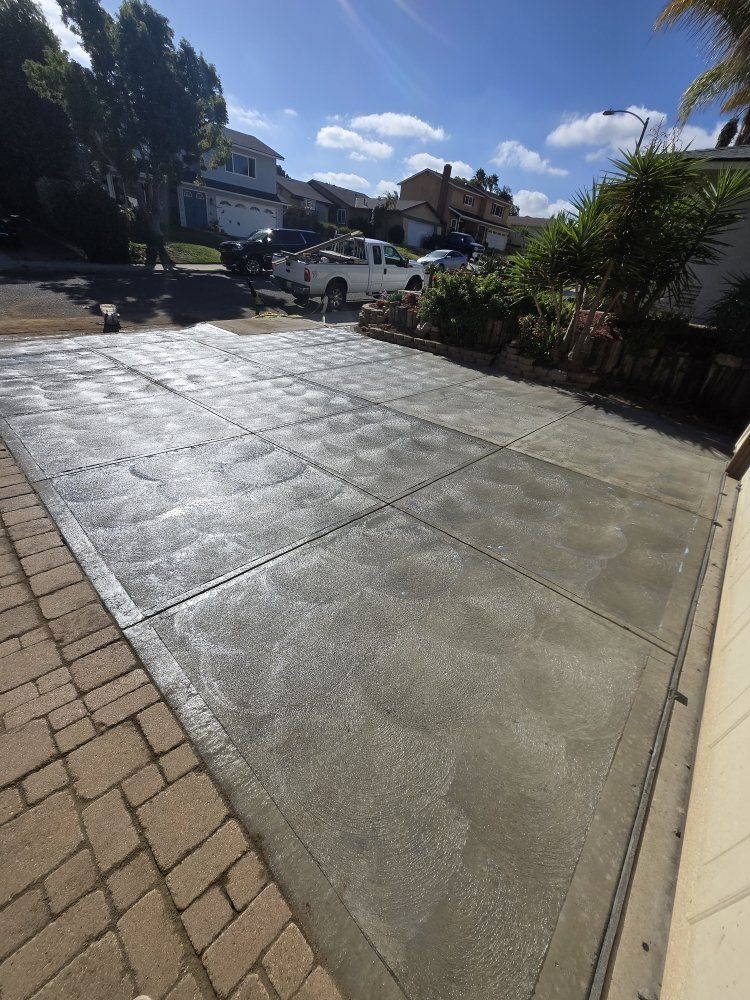 Newly poured concrete driveway with grid pattern; adjacent to a brick-paved area; sunny outdoor setting.