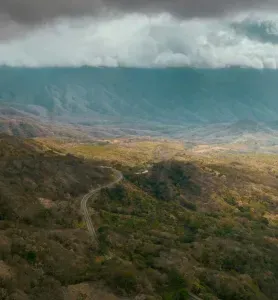 Rolling mountain landscape with a winding road through a valley, under cloudy skies.