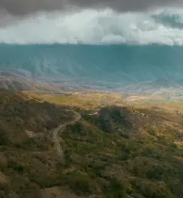Rolling mountain landscape with a winding road through a valley, under cloudy skies.
