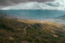 Rolling mountain landscape with a winding road through a valley, under cloudy skies.