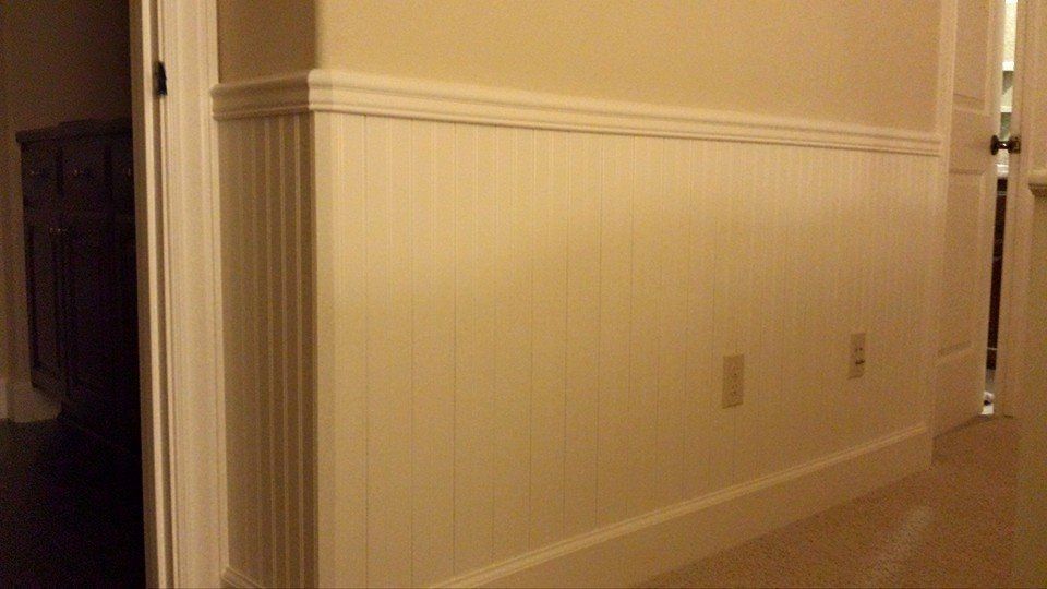 A hallway with white wainscoting on the walls and a door.