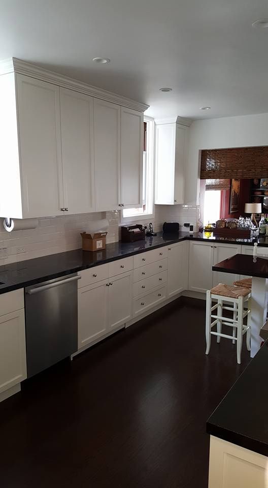 A kitchen with white cabinets, black counter tops, and a stainless steel dishwasher.