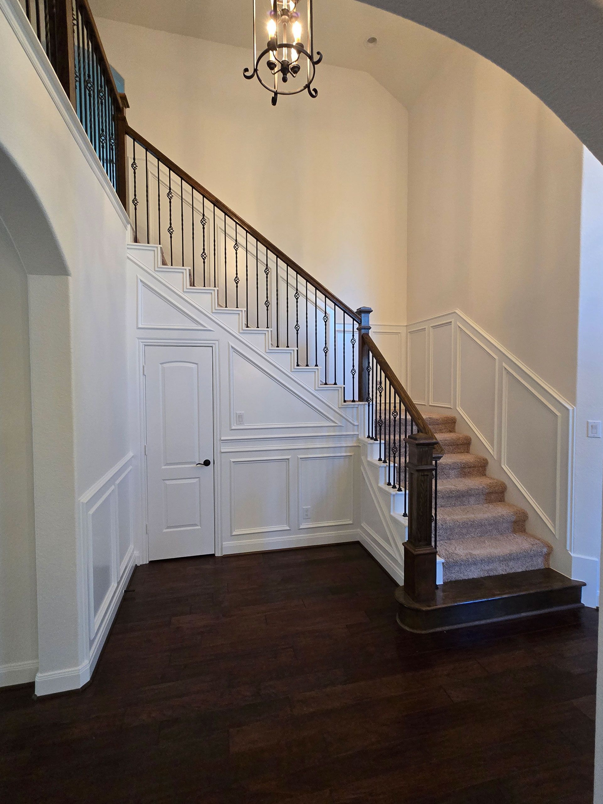 Interior view of a staircase with dark wooden floors and a white paneled wall.