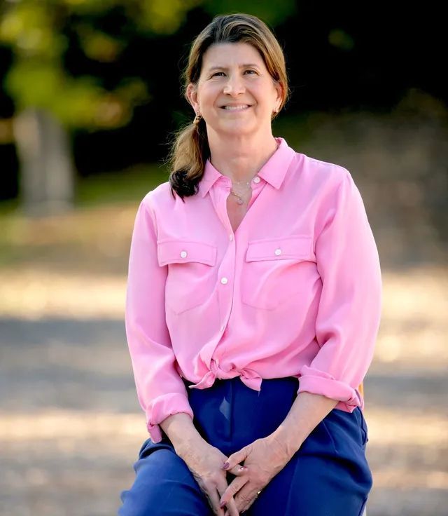 A woman in a pink shirt and blue pants smiles for the camera