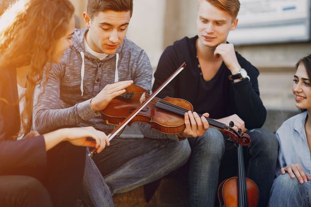 A group of young people are sitting on the ground playing violins.