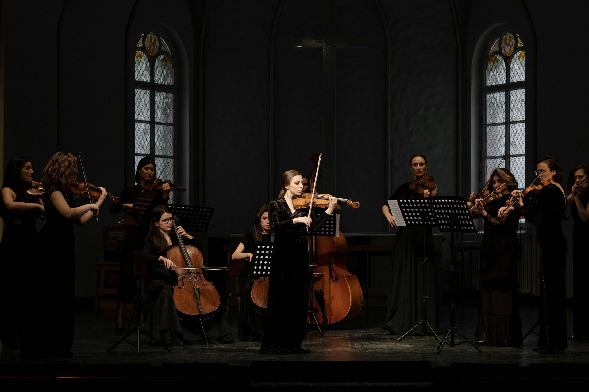 A group of women are playing violins and cello in a dark room.