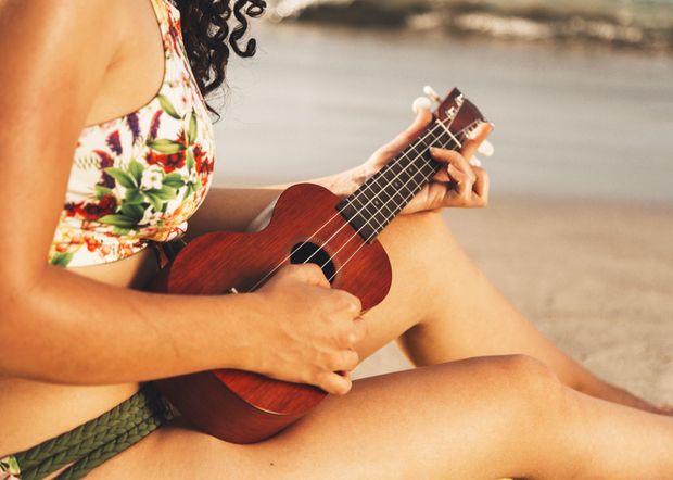 A woman in a bikini is sitting on the beach playing a ukulele.