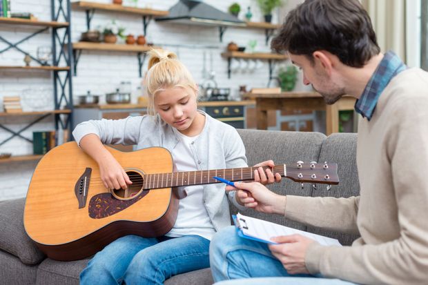 A man is teaching a young girl how to play an acoustic guitar.