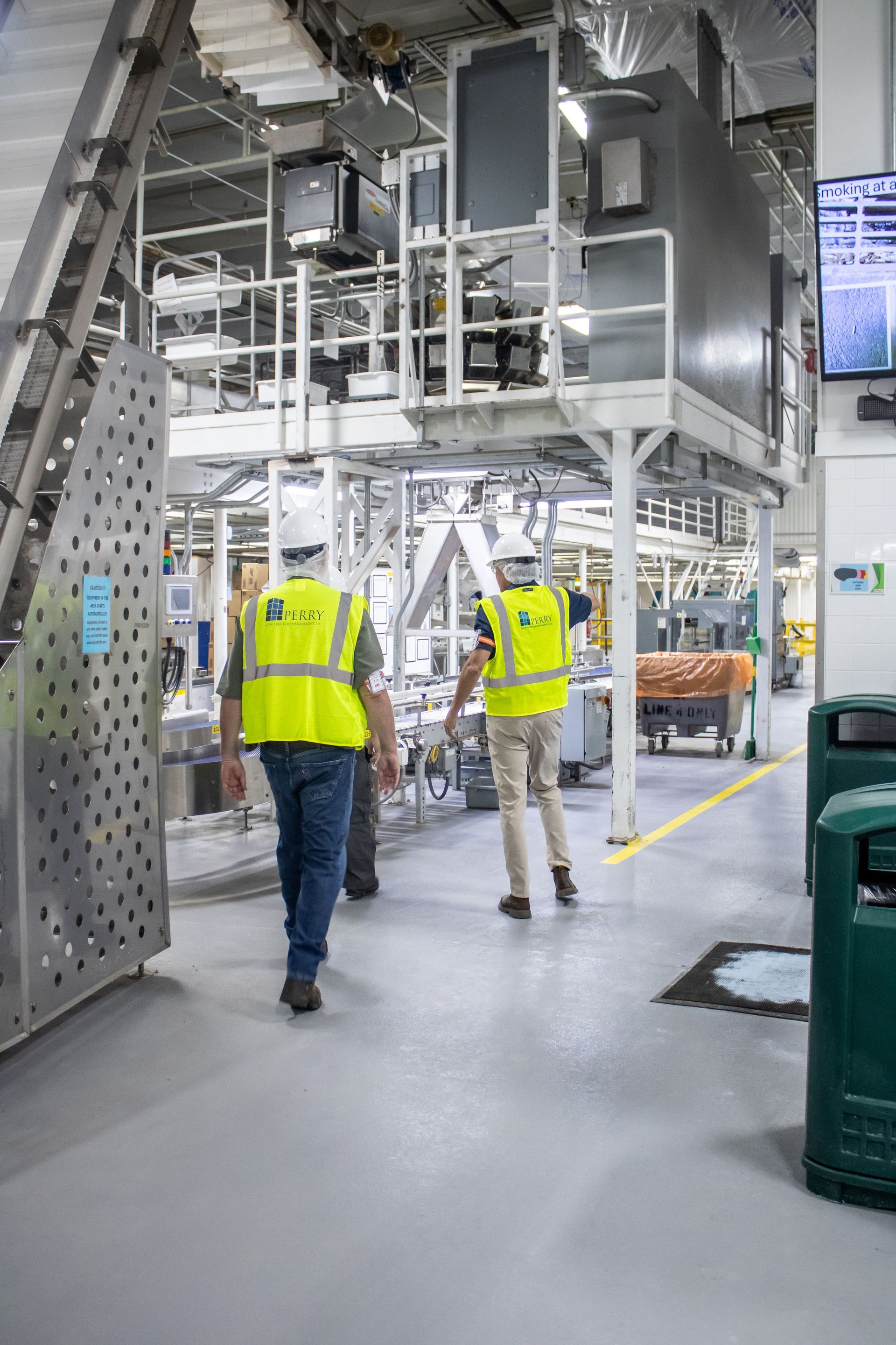 Two workers in safety vests walking through a food processing factory.