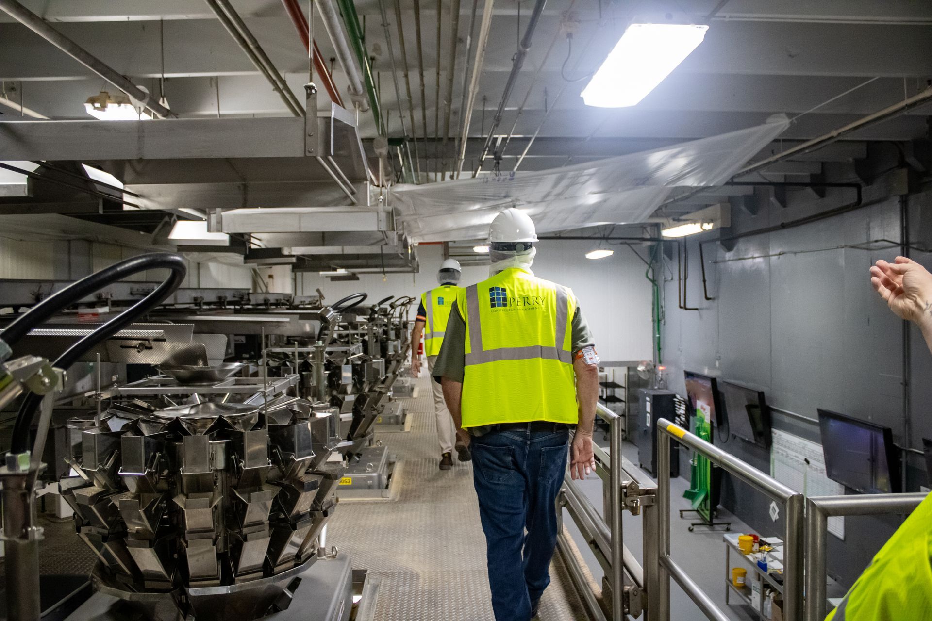 Workers in safety vests walk through a food processing facility, next to automated machinery.
