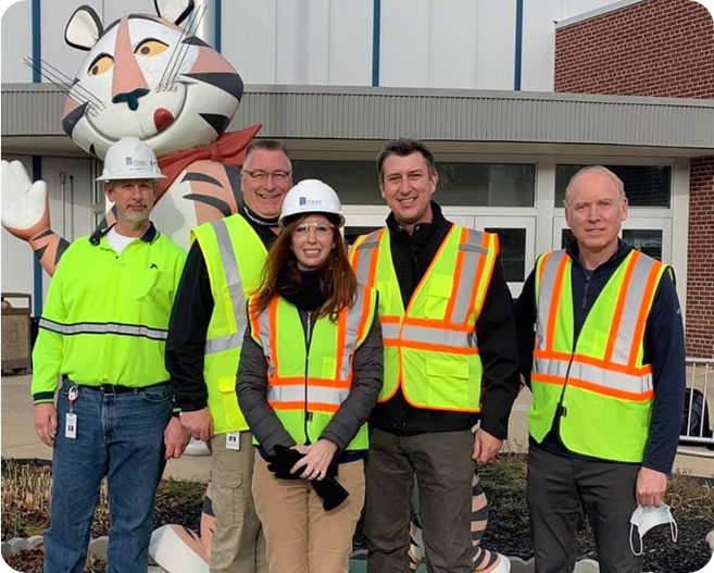 Two men in safety vests shake hands in front of a white building.