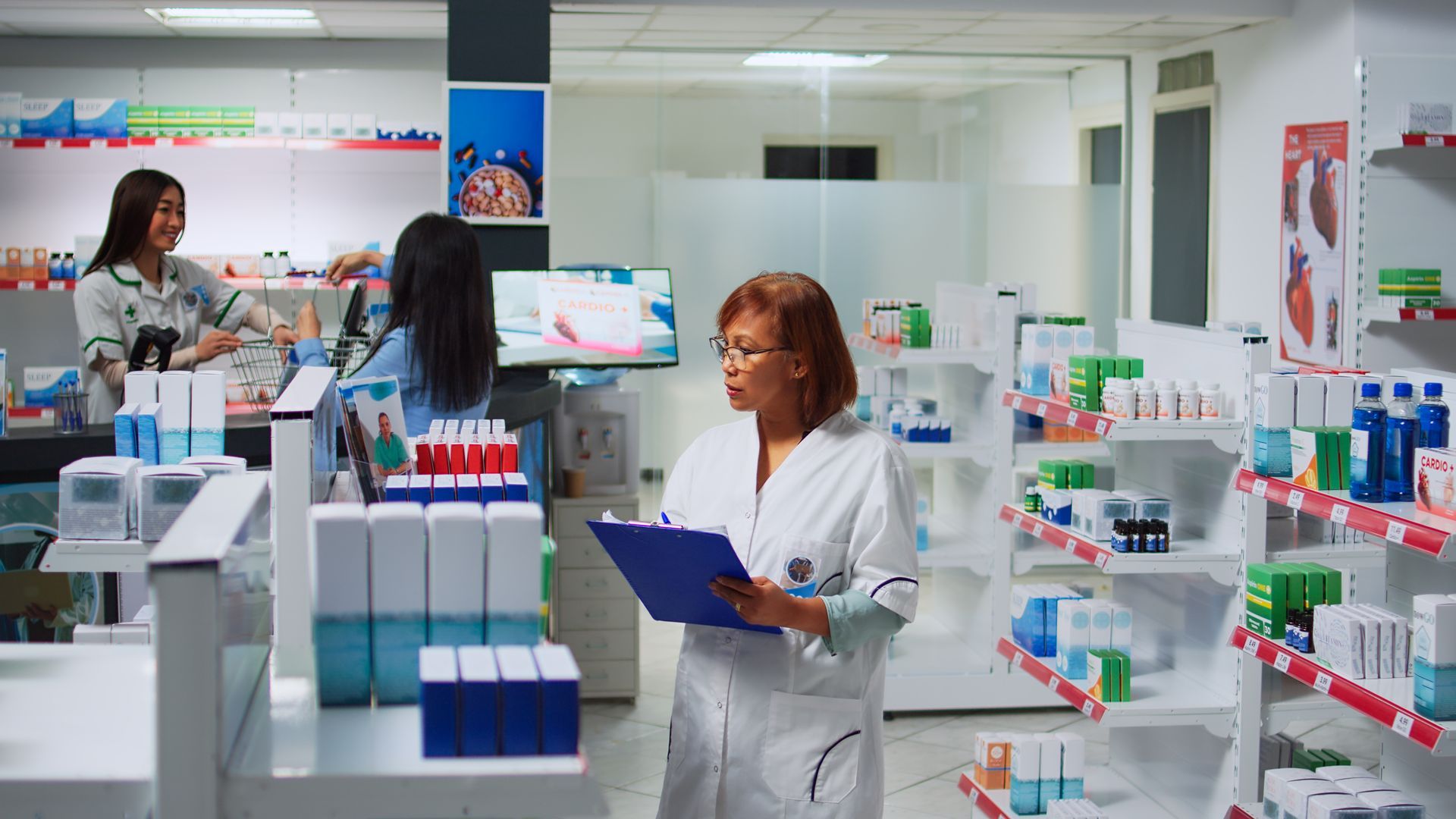 Pharmacy interior; pharmacist in white coat reviews clipboard, looking at shelves of medications.