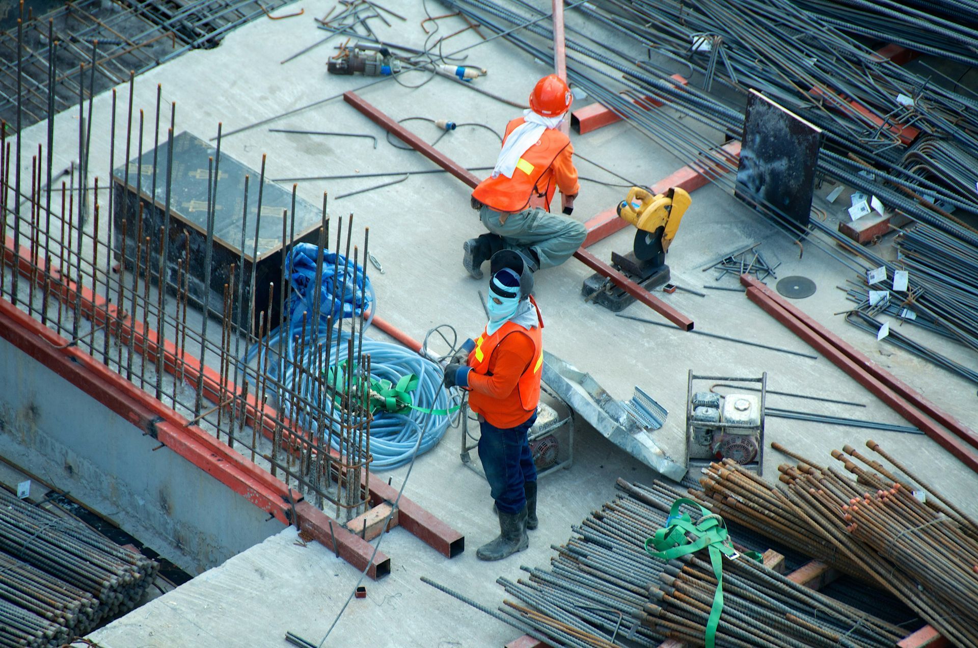 Construction workers welding rebar on a concrete structure, wearing orange vests and hard hats.