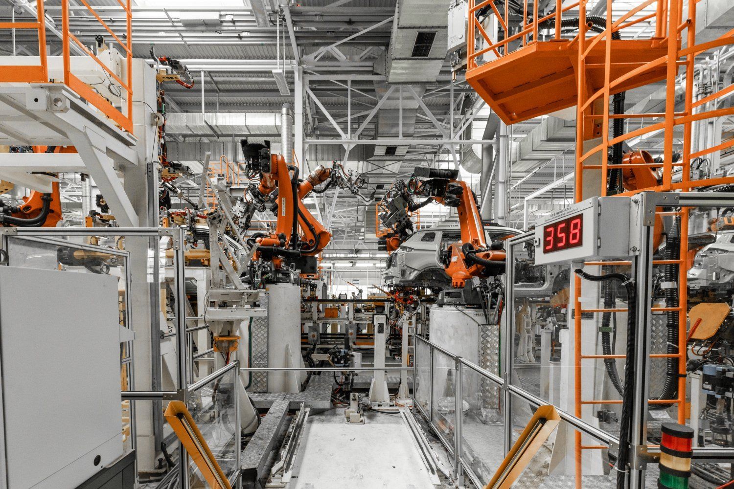 Robotic arms in a car factory, welding and assembling car bodies. Orange and gray machinery, industrial setting.