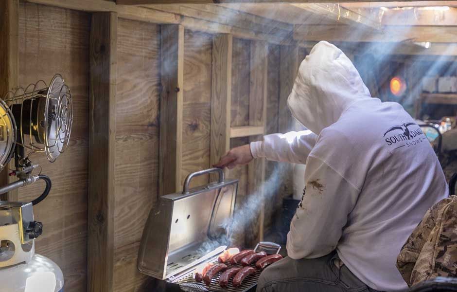 A man is cooking sausages on a grill in a shed.