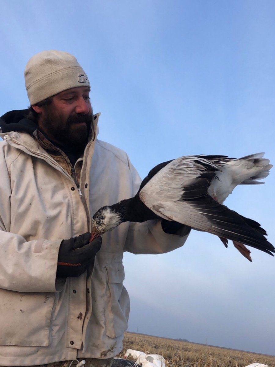 A man in a white jacket is holding a black and white bird