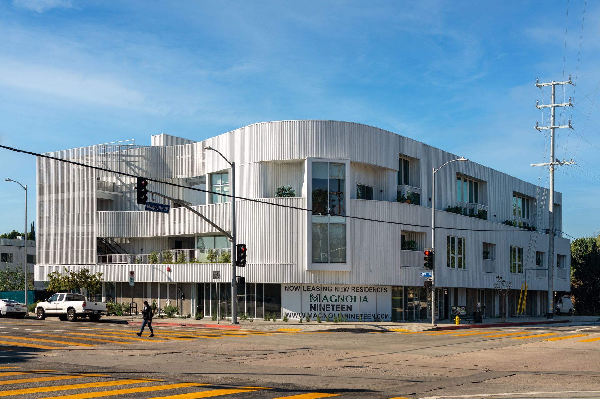 A large white building is sitting on the corner of a city street.