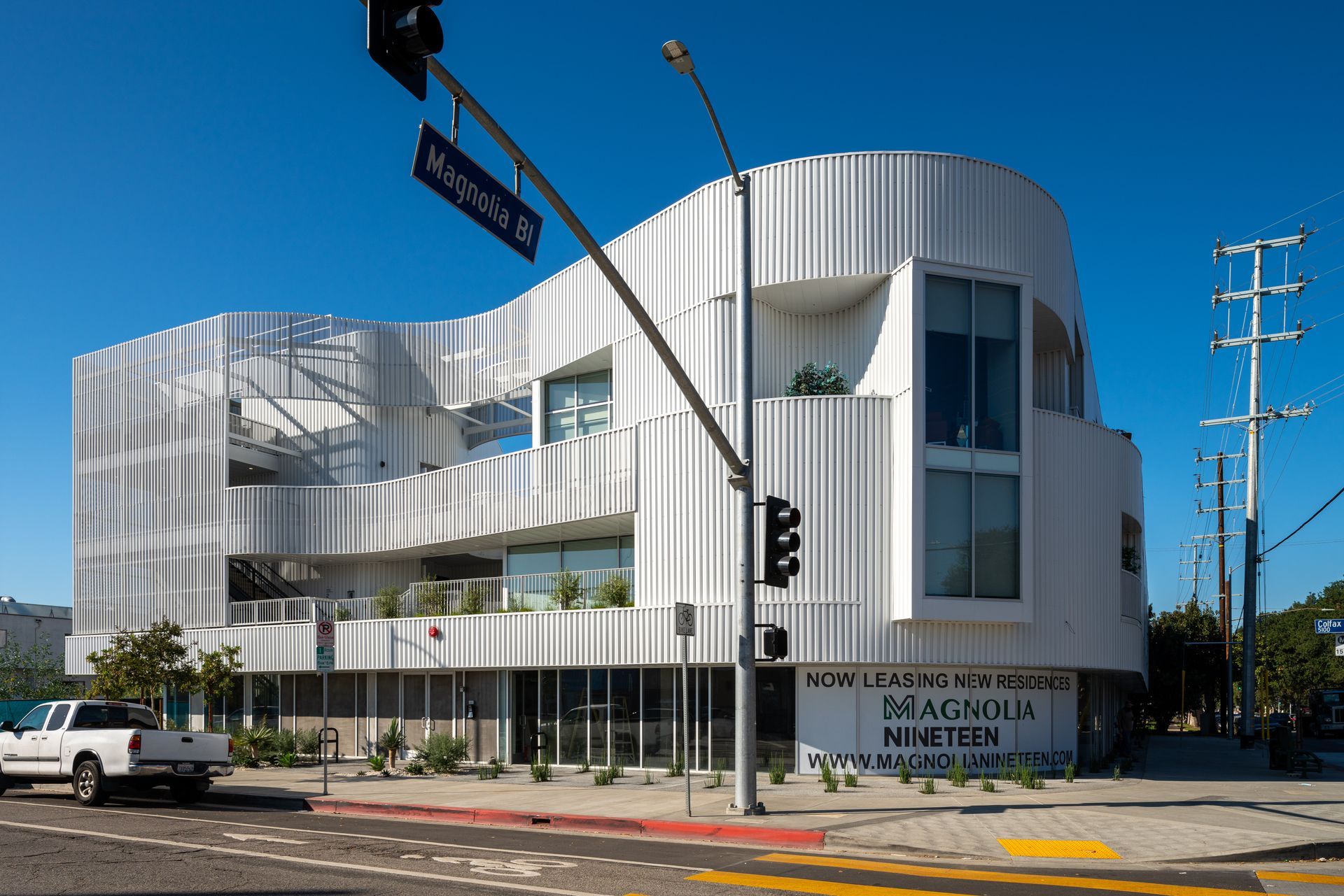 A white truck is parked in front of a large white building.