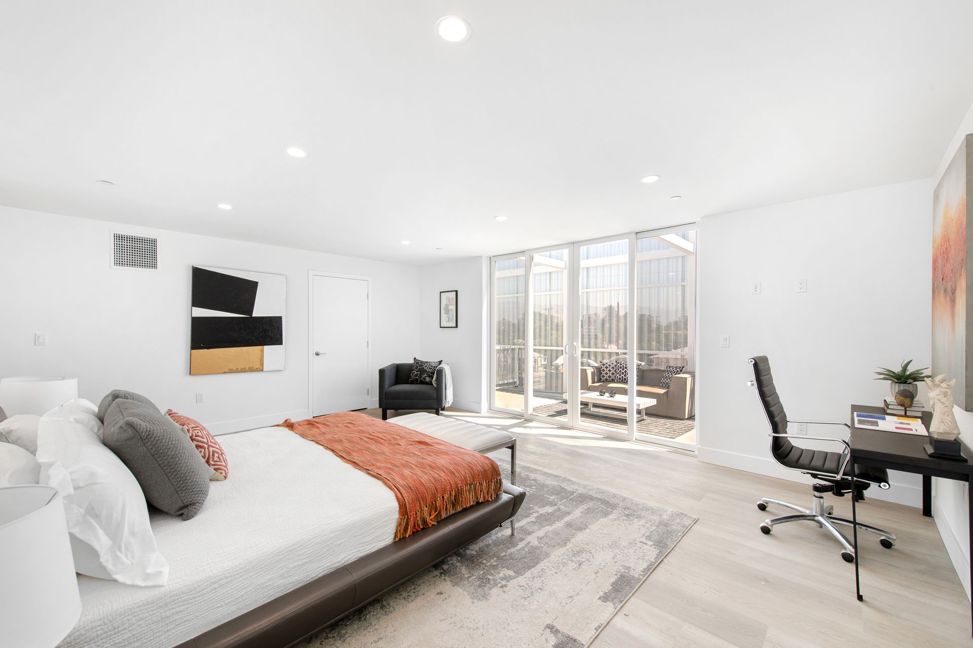 A bedroom with a large bed , desk , chair and sliding glass doors.