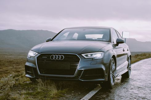 A black audi is parked on the side of a wet road.