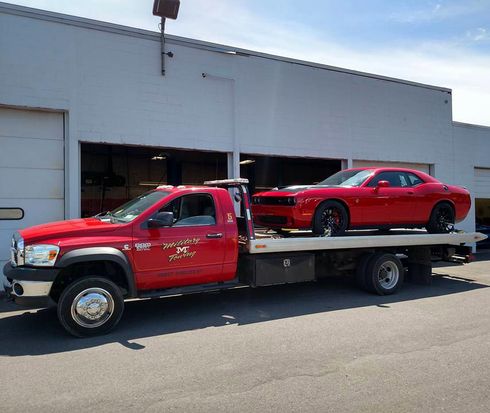 A red tow truck with a red car on the back of it