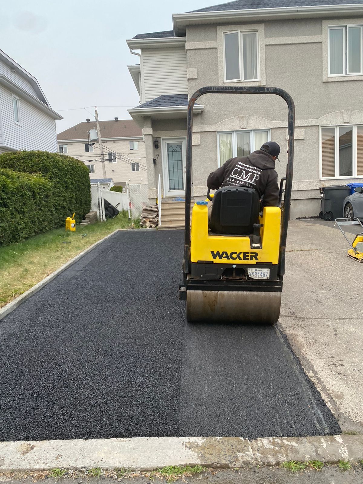 Un homme conduit un rouleau compresseur sur une allée devant une maison.
