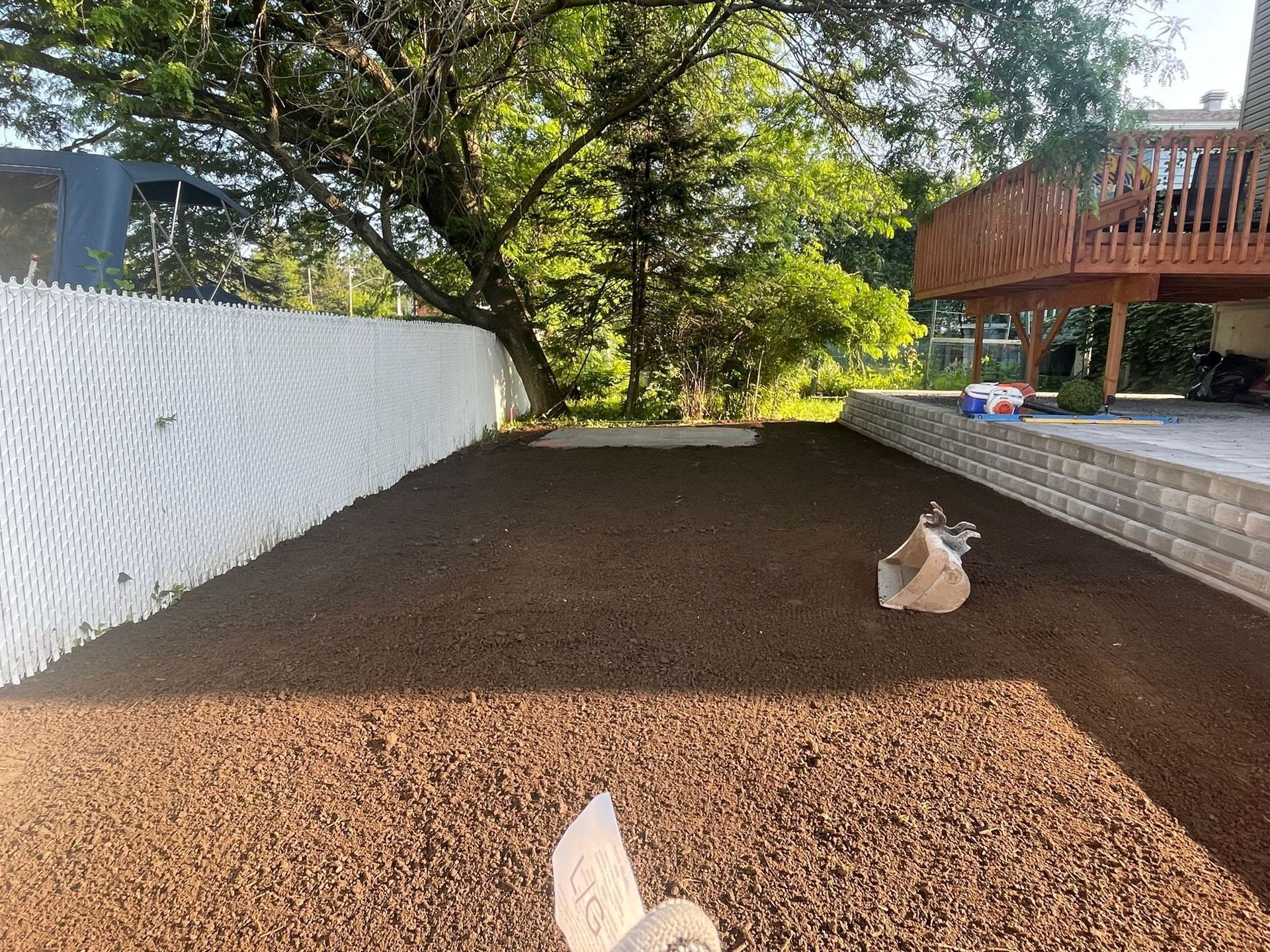 Une pelouse avec une clôture blanche et une terrasse en arrière-plan.