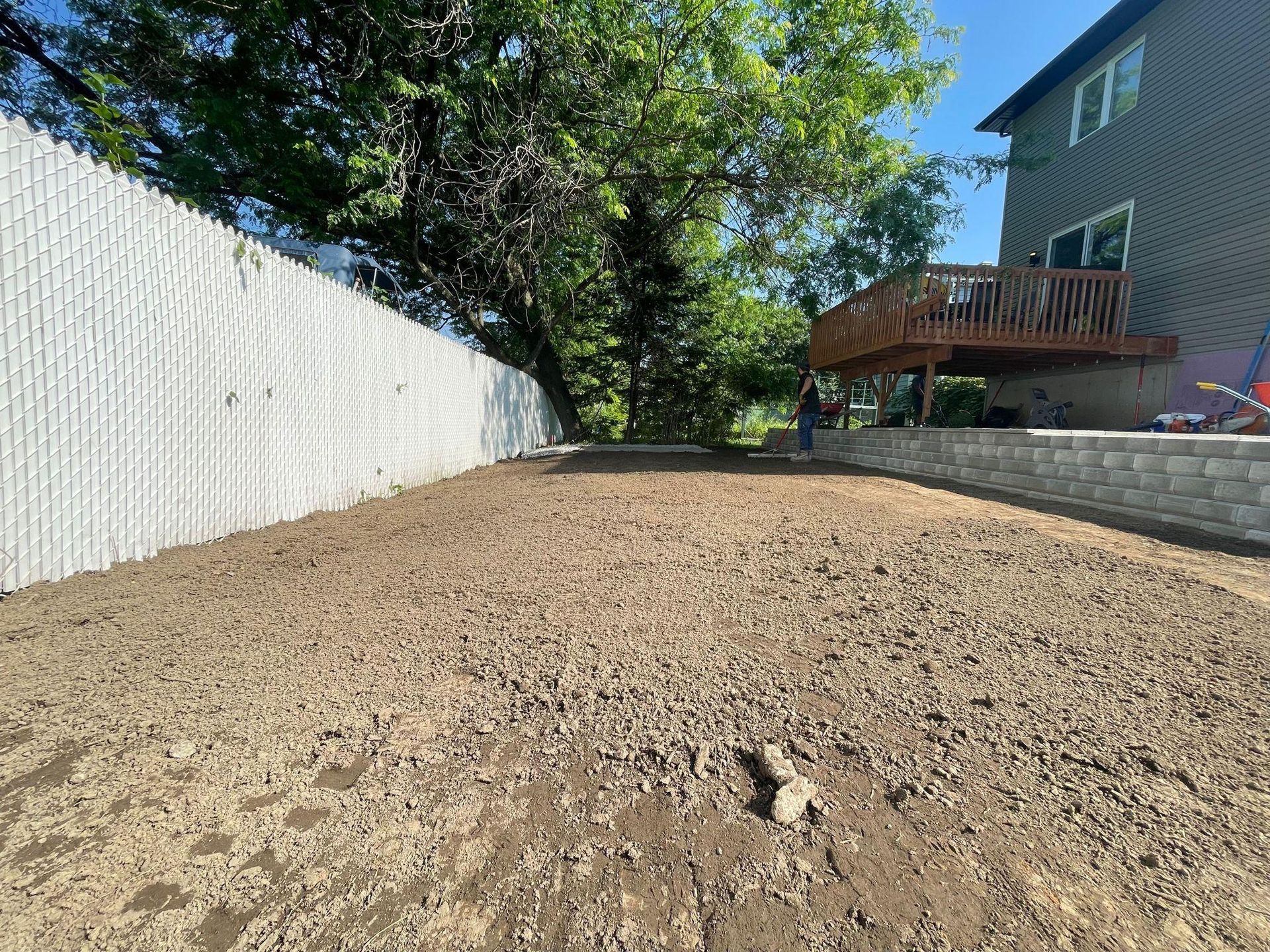 Une cour arrière avec une clôture blanche et une terrasse en arrière-plan.