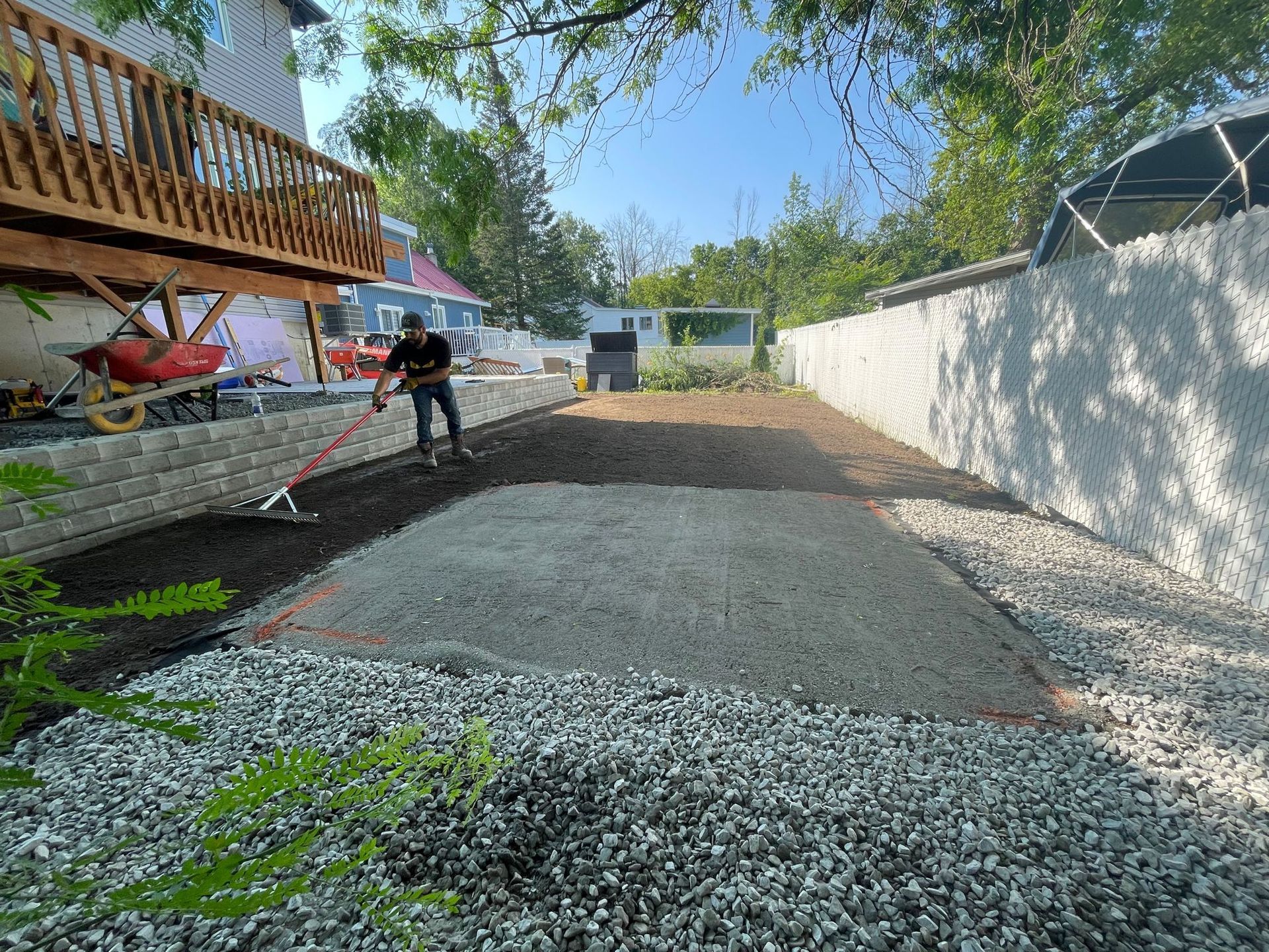 Un homme ratisse du gravier dans une allée devant une maison.