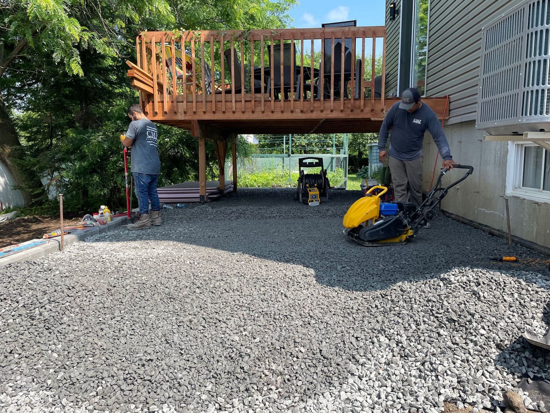 Deux hommes travaillent sur une allée de gravier devant une maison.