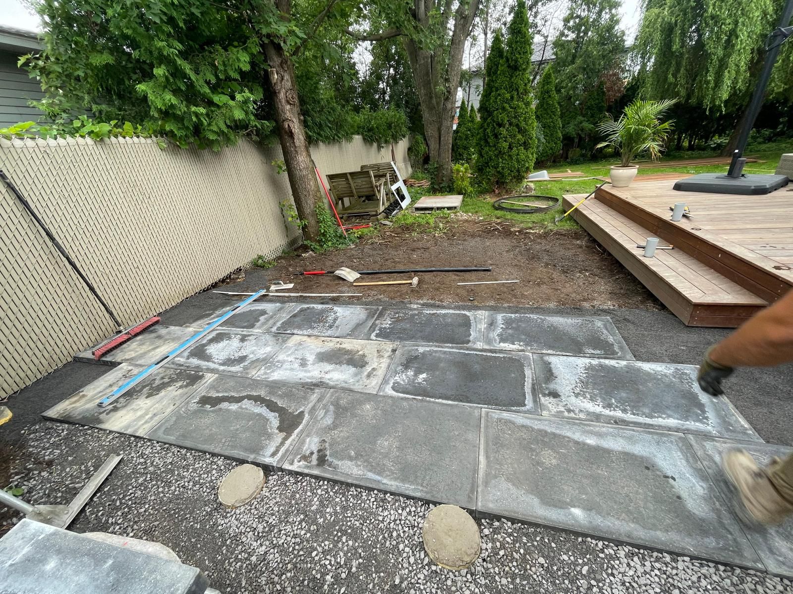 Une personne pose des carreaux sur une terrasse dans une cour arrière.